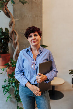 Confident business woman holding laptop standing in office