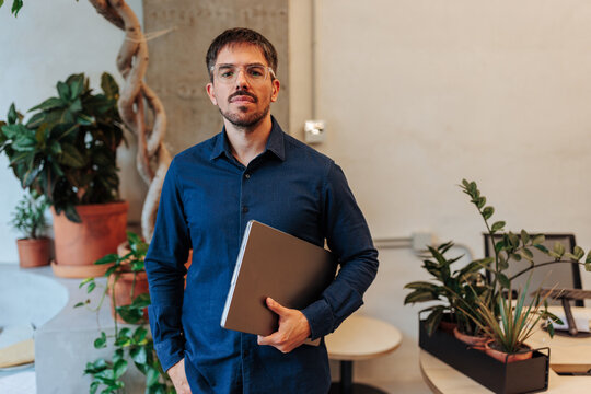 Man holding laptop standing in modern office environment