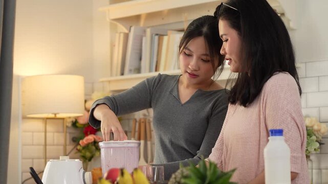 Friends making fresh fruit smoothies using a blender at home, Two young women preparing a healthy smoothie together in modern kitchen, Happy women blending healthy drinks in a bright domestic kitchen