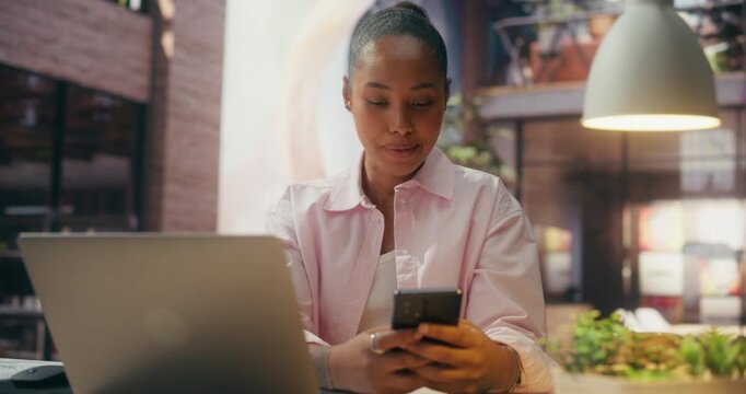 360 Degree. Concentrated Black Businesswoman Syncs Smartphone and Laptop at Office Desk, Reviewing Ecommerce Notifications, Optimizing Digital Workflow and Boosting Online Sales. Arc Tracking Shot.