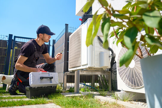 HVAC technician checking outdoor heat pump unit with tool