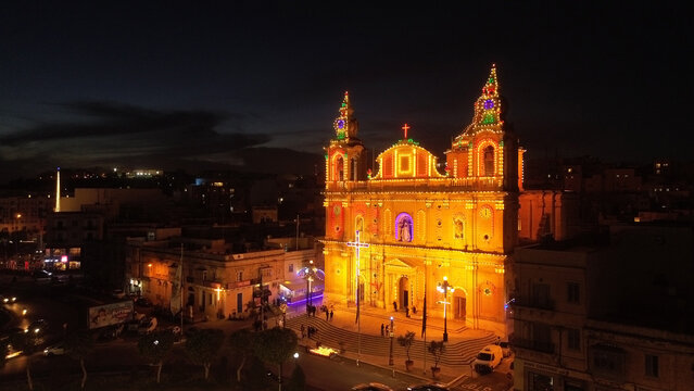 Aerial view of an illuminated church facade decorated with festive lights at night in the city center of Valletta, Port Region, Malta.