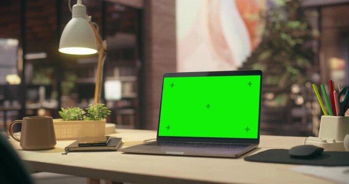 Green Screen Chroma Key Laptop Resting on Wooden Desk Beside Coffee Mug Loft Office. Blank Mockup Display Ready for Business App, Website or Software Presentation. Slow Arc Camera Move.