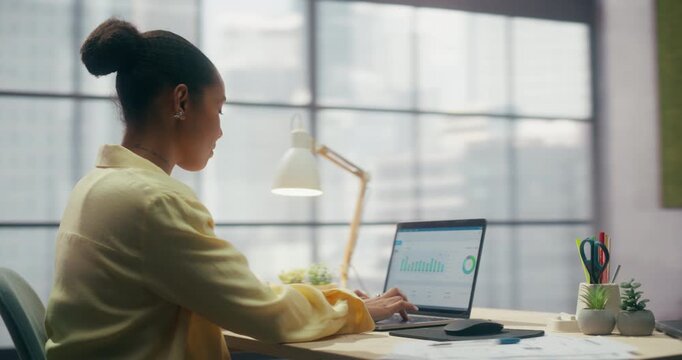 360 Degree. Confident Black Businesswoman Types on Laptop in Cozy Loft Office, Managing Ecommerce Sales Dashboard, Boosting Productivity and Driving Online Business Success. Cinematic Tracking Shot