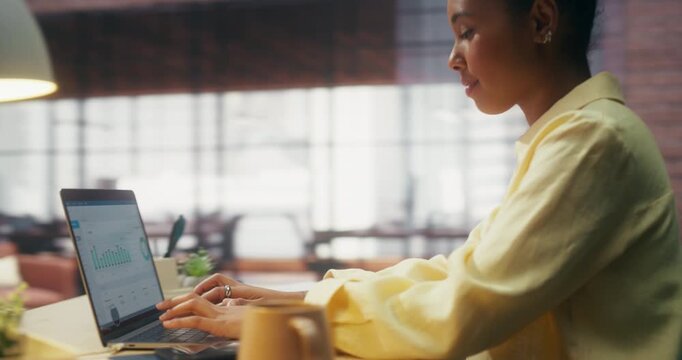360 Degree. Smiling Black Woman Works on Laptop in Loft Office, Monitoring Ecommerce Dashboard, Analyzing Digital Marketing Metrics and Achieving Online Business Growth. Cinematic Arc Tracking Shot.