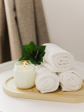 Minimalist still life of luxury spa essentials. White cotton towels with soy wax candle on a table.