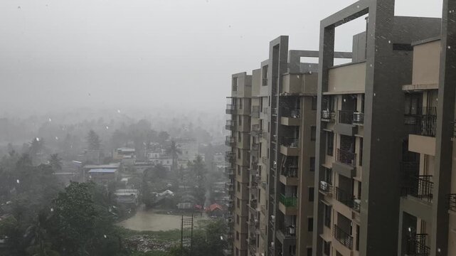 A highangle view of intense monsoon rainfall over a residential apartment complex and a lush tropical town in India. Perfect for weather reports or climate documentaries.