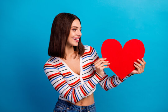 Young woman holds red heart against blue background smiling in a cheerful lifestyle scene