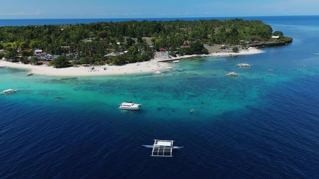 Drone pulls back and tilts up to reveal Pamilacan Island, boats, beach, reef, and blue water in Bohol