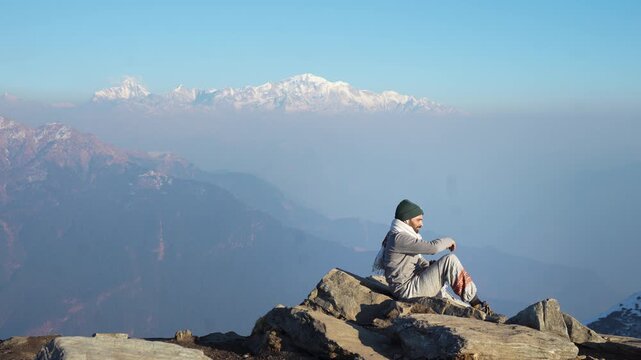 Silhouette of Pilgrim Sitting on Mountain Peak Overlooking Himalayan Ranges at Sunrise Tungnath Temple, Uttarakhand, India