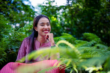 Naklejka premium Portrait of a young woman smiling gently surrounded by lush green ferns and vibrant foliage.