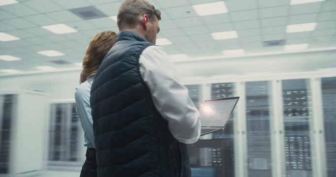 360 Degree. Male and Female It Specialists Review AI Software on Laptop While Standing Among Server Racks in a Data Center, Discussing Network Performance and System Optimization. Arc Tracking Shot.