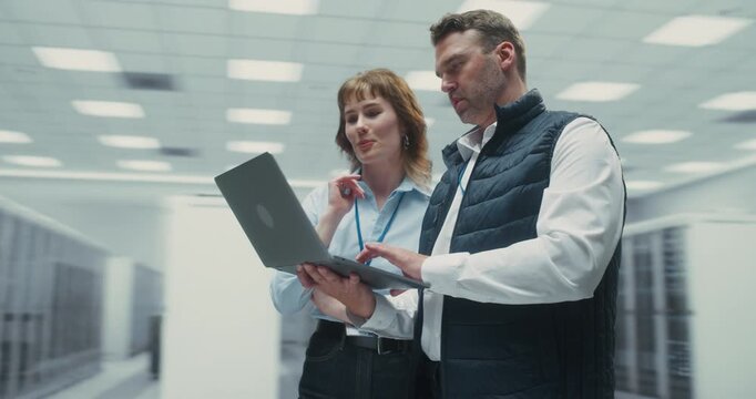360 Degree. Male and Female Engineers Collaborate on Laptop Analyzing AI Data Among Server Racks in a Data Center, Cloud Network Systems and Digital Infrastructure. Cinematic Arc Tracking Shot.