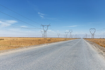 Obraz premium Desert Highway Stretching Toward Distant Transmission Towers Under Clear Blue Sky