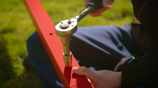Close up mechanic tightening bolt with socket wrench on painted steel bar. Assembly repair activity with metal parts and fastening tool in natural light. Industrial maintenance concept with technician