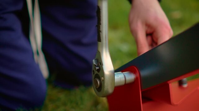 Precision ratchet tightening metal joint on red bracket and black beam outdoors. Close-up mechanical fastening with socket wrench and steady hand control. DIY construction concept with accurate torque