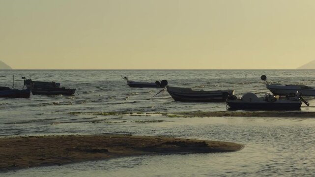 Fishing Boats Floating On Sea Water Near Sandy Shore At Sunset. Calm Evening 