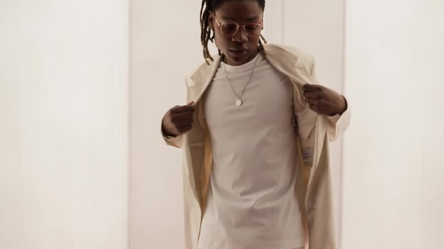 Slowmo shot of talented young African American man adjusting stylish jacket and gesturing while performing in white narrow corridor. Perfect for diversity marketing fashion campaigns