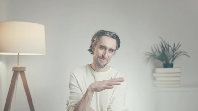 Young man making so so gesture while speaking indoors, uncertainty and mixed opinion concept