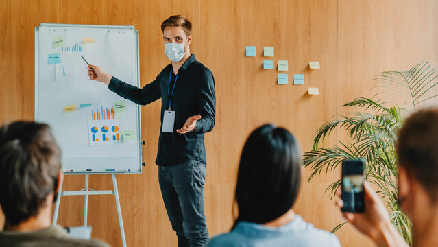 Business speaker in mask discussing project ideas with team during presentation in conference room, corporate training seminar, professional communication, business education and teamwork concept
