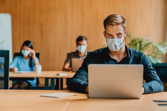 Young man with laptop computer wearing protective medical mask while working in office, businessman protected from virus disease, healthcare safety measures, pandemic workplace business concept