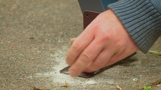 Close perspective of ratchet driving screw into concrete anchor fixing metal base plate. Hand stabilizing hardware while tool applying rotational force for tight connection. Construction process