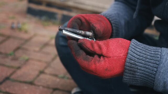 Gloved hands comparing new and worn brake caliper guide pins during brake maintenance. Close up DIY automotive repair examining replacement and damaged caliper components before reassembly. Vehicle