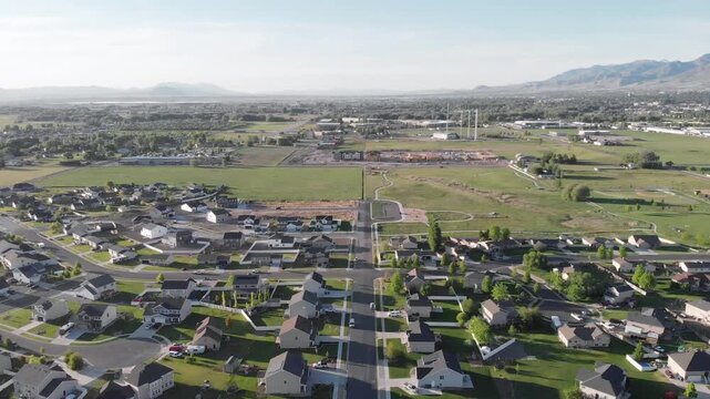 Aerial view of a quiet suburban neighborhood in cache valley utah with houses, green fields, and mountains in the background under a clear sky.