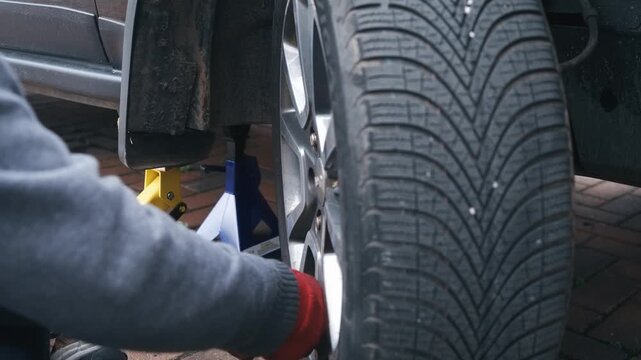 Wheel lug nuts hand fastening during passenger car wheel installation. Gloved mechanic threading fasteners onto alloy rim after brake repair and wheel mounting. Automotive reassembly process and