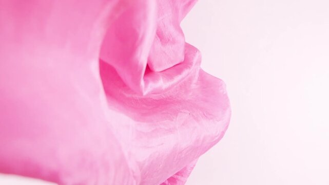 Pink silk fabric slowly falls onto a white background in slow motion. Elegant folds and soft satin waves create a premium texture ideal for fashion projects, luxury branding, and cosmetics advertising