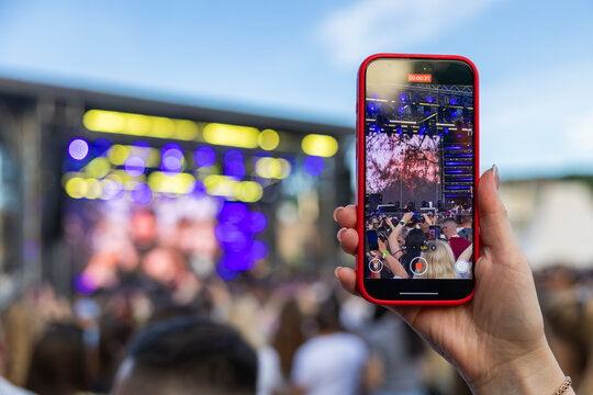 Hand holding smartphone recording video of live concert music festival stage