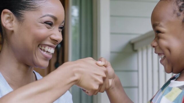 Reaching woman and son clasping hands on front porch, bonding, wearing light top and striped shirt