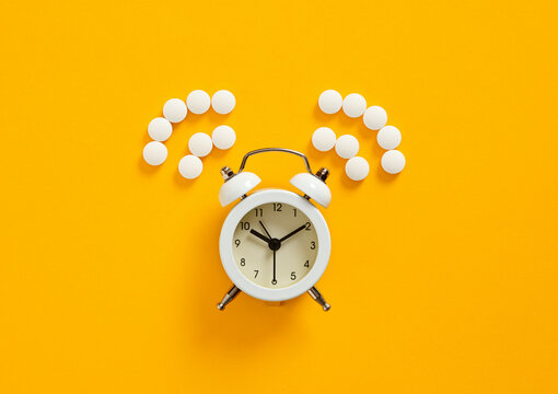 White alarm clock and pills forming question marks on yellow background