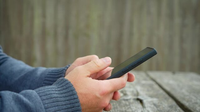 Messaging smartphone communication on wooden backyard table near garden fence. User browsing notifications responding to chats and using social media applications. Mobile technology lifestyle focused