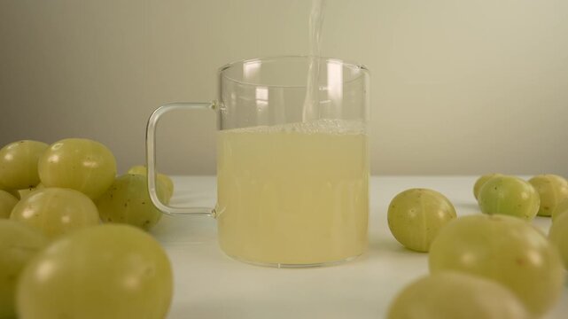 Fresh Indian gooseberry juice pouring into a glass cup. Amla juice. Phyllanthus emblica.