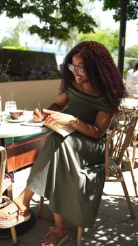 Young woman in a cafe outdoors writing in a notebook on a sunny day