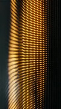 Vibrant macro shot of a digital LED display featuring a grid of bright orange and yellow lights in a geometric arrangement. Perfect for tech, innovation, and digital design themes