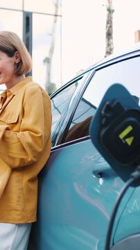 Adult woman using a mobile application on smartphone to charge an electric car at an outdoor parking lot. Concept of smart charging technology, electric vehicles, clean energy, sustainable
