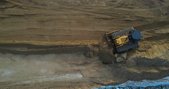 Top-down aerial view of a yellow bulldozer leveling sand and leaving detailed track marks at a construction site