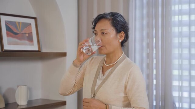 Smiling mature grandmother holds glass of water to drinking for healthcare or natural vitamins in house, attractive old woman relaxing or thirsty, drink pure mineral water for body hydration energy