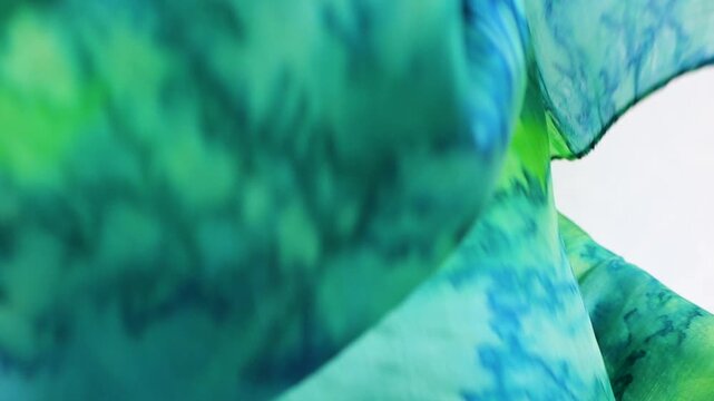Green and blue silk fabric falls onto a white background. This elegant flowing textile creates a beautiful moving canvas suitable for luxury fashion and commercial branding.