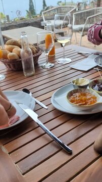 Delicious gourmet brunch buffet or appetizer spread on a rustic wooden outdoor table featuring cheese platters, charcuterie, fresh fruit cups, sweet berry panna cotta desserts, and white wine glasses