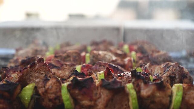 Pork meat skewers with zucchini and tomato slices cooking on charcoal grill with rising smoke. Close up barbecue footage with shallow depth of field. Outdoor summer cooking and picnic concept. 