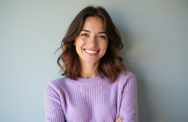 Obraz premium Smiling brunette woman with brown hair wears lilac sweater. She looks at the camera with a happy expression. Her arms are crossed in front of her body. Studio portrait.