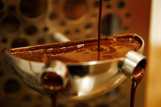 Melted liquid chocolate pouring into metal bowl of fountain