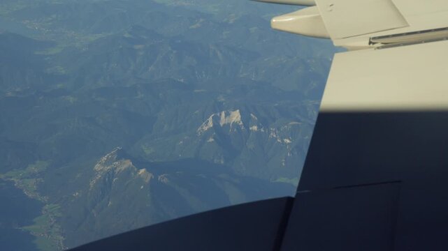 A video shot from an airplane window showcasing a broad view of green mountain ridges and rocky peaks beneath the aircraft's wing during a flight toward Tirana.