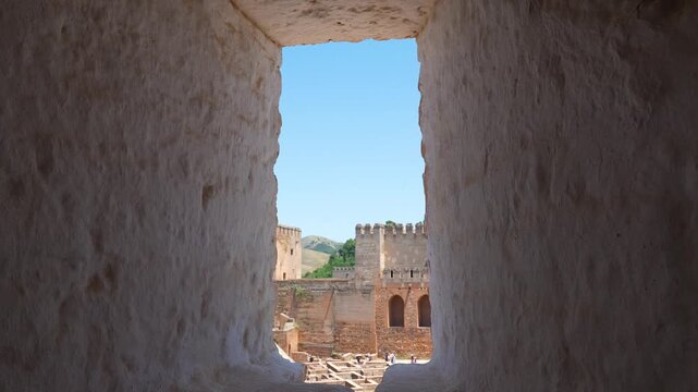 View of the Alcazaba fortress inside the Alhambra complex in Granada, Spain framed through a narrow medieval stone window