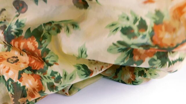 Lightweight silk scarf with orange floral pattern falls onto a white background. Soft fabric creates elegant folds. This high-quality textile material is perfect for luxury fashion commercials.