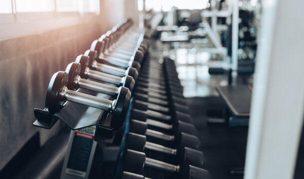 fitness concept. Dumbbell row in gym fitness room with metal weight rack and soft sunlight