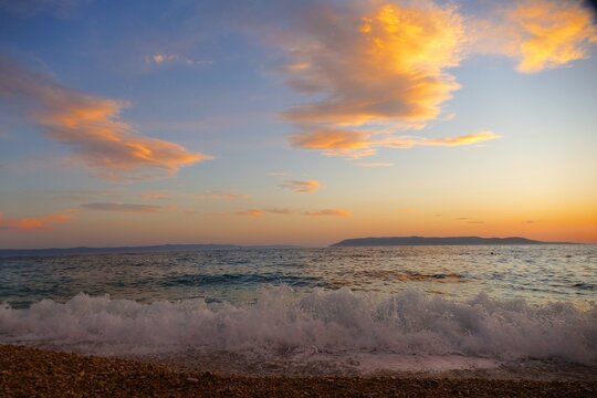 Waves on the wind with foam on the sea horizon with colorful clouds in sunset summer sunset background